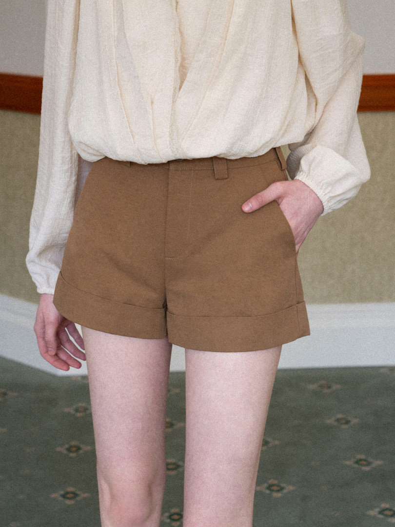Model wearing brown high-waisted tailored shorts with a cream blouse