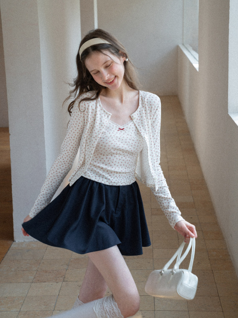 Woman wearing a patterned cardigan and top with a navy skirt, holding a white handbag