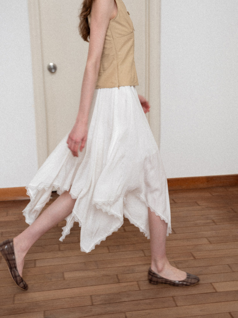 Model wearing a tan sleeveless top with a flowing white skirt and plaid flats