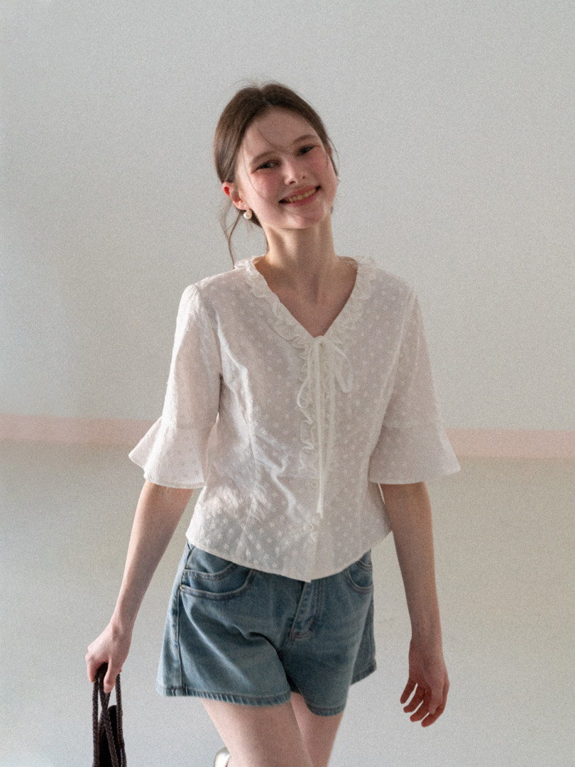 Model wearing a white ruffled short-sleeve blouse with blue denim shorts