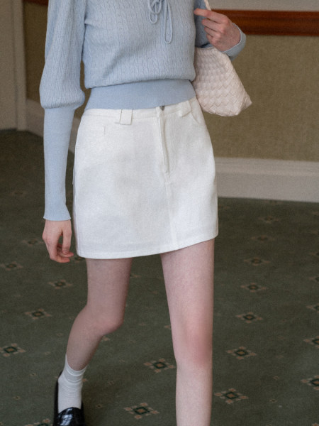 Model wearing a light blue knit top with a white mini skirt and woven bag