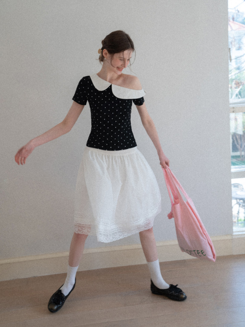 Model wearing a black polka dot off-shoulder top with a white skirt