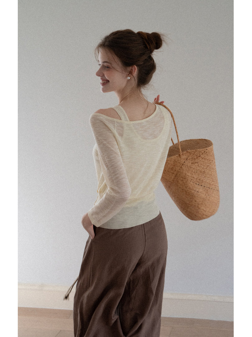 Model wearing a sheer cream top with brown pants and a woven straw tote bag