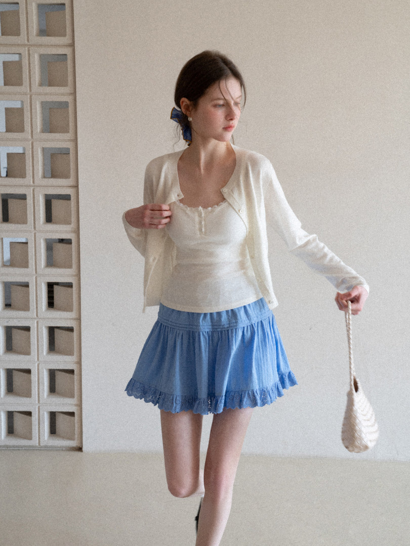 Model wearing a cream cardigan and top with a blue ruffled mini skirt