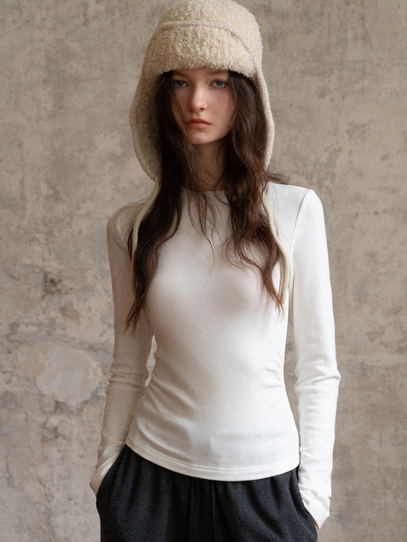 Model wearing a fitted white long-sleeve top and dark pants with a soft hat