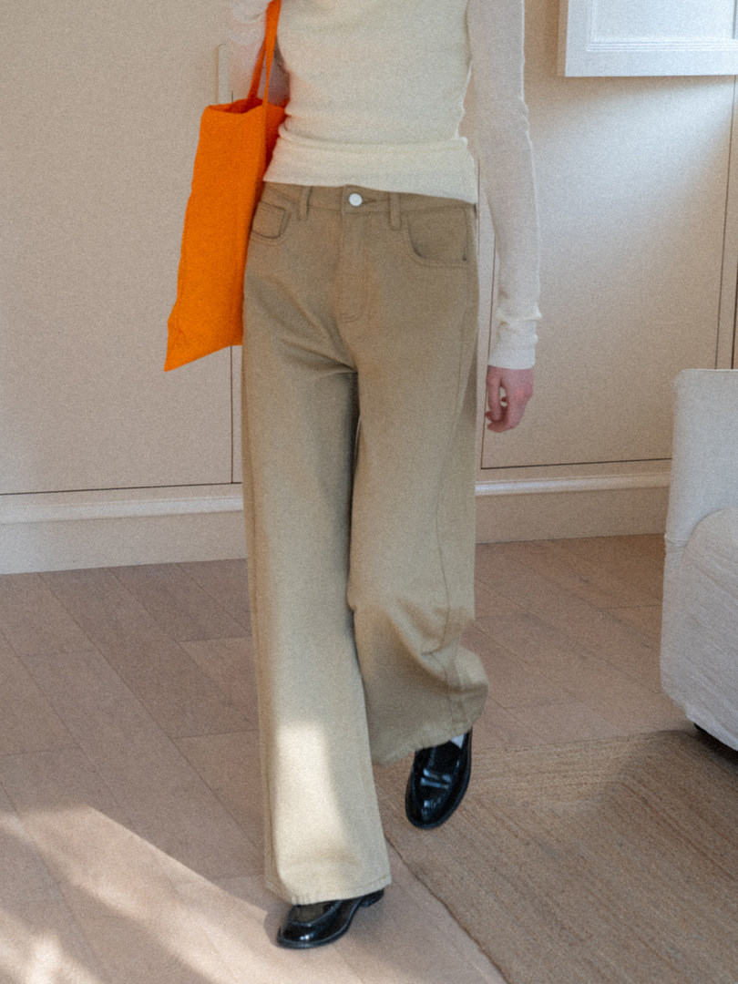 Model wearing beige wide-leg trousers with a white top, orange shoulder bag, and black loafers