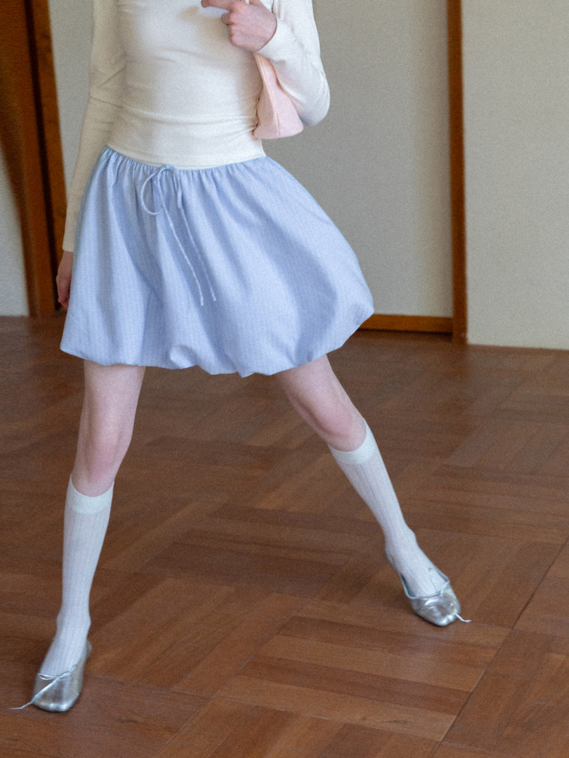Model wearing a light blue skirt with a white top and silver flats