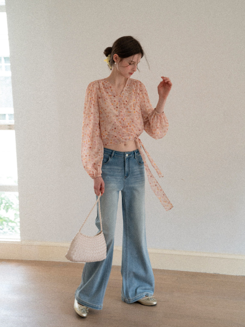 Woman wearing a floral tie-front blouse with wide-leg jeans and a woven shoulder bag