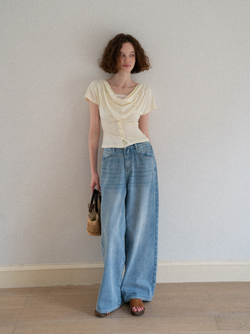 Model wearing a cream draped short-sleeve top with light blue wide-leg jeans