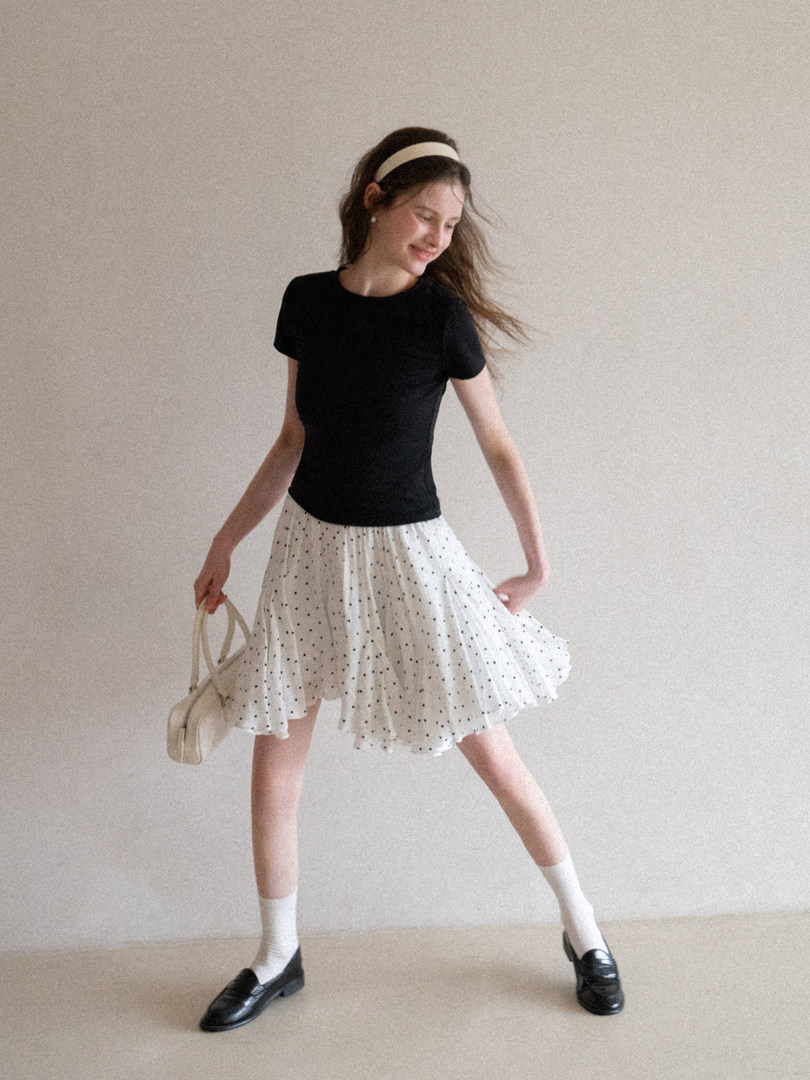 Woman wearing a black short-sleeve top with a white polka dot skirt and loafers