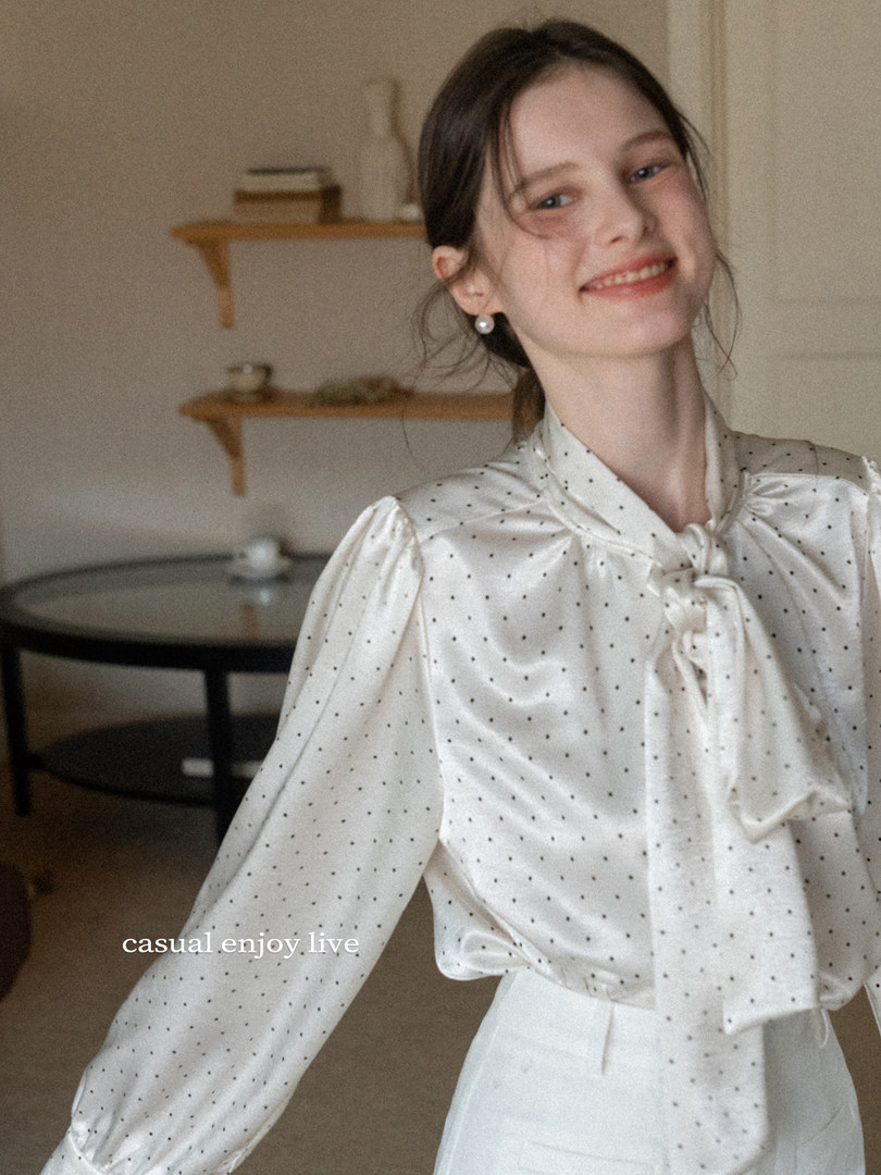 Woman wearing a white polka dot satin blouse with a bow tie collar
