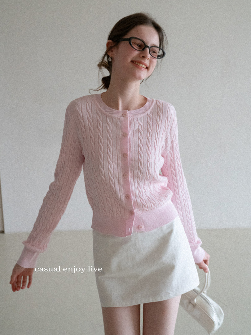 Woman wearing a pink cable-knit cardigan and white skirt