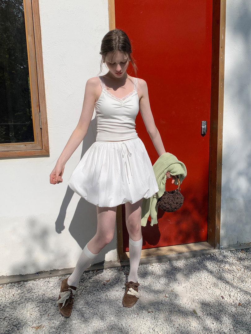 Woman wearing a white sleeveless top and white bubble skirt outdoors