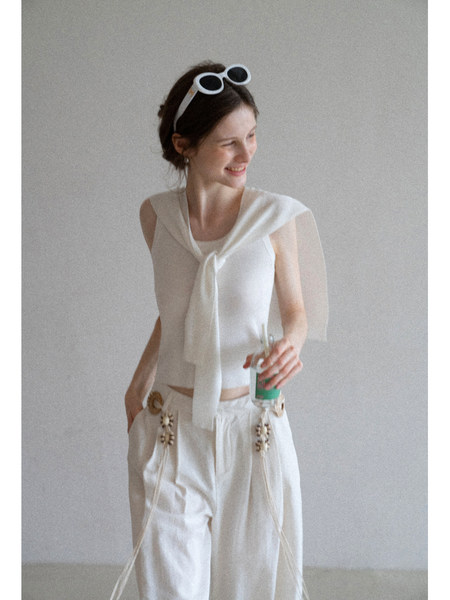 Model wearing a white sleeveless top and white wide-leg pants with decorative details