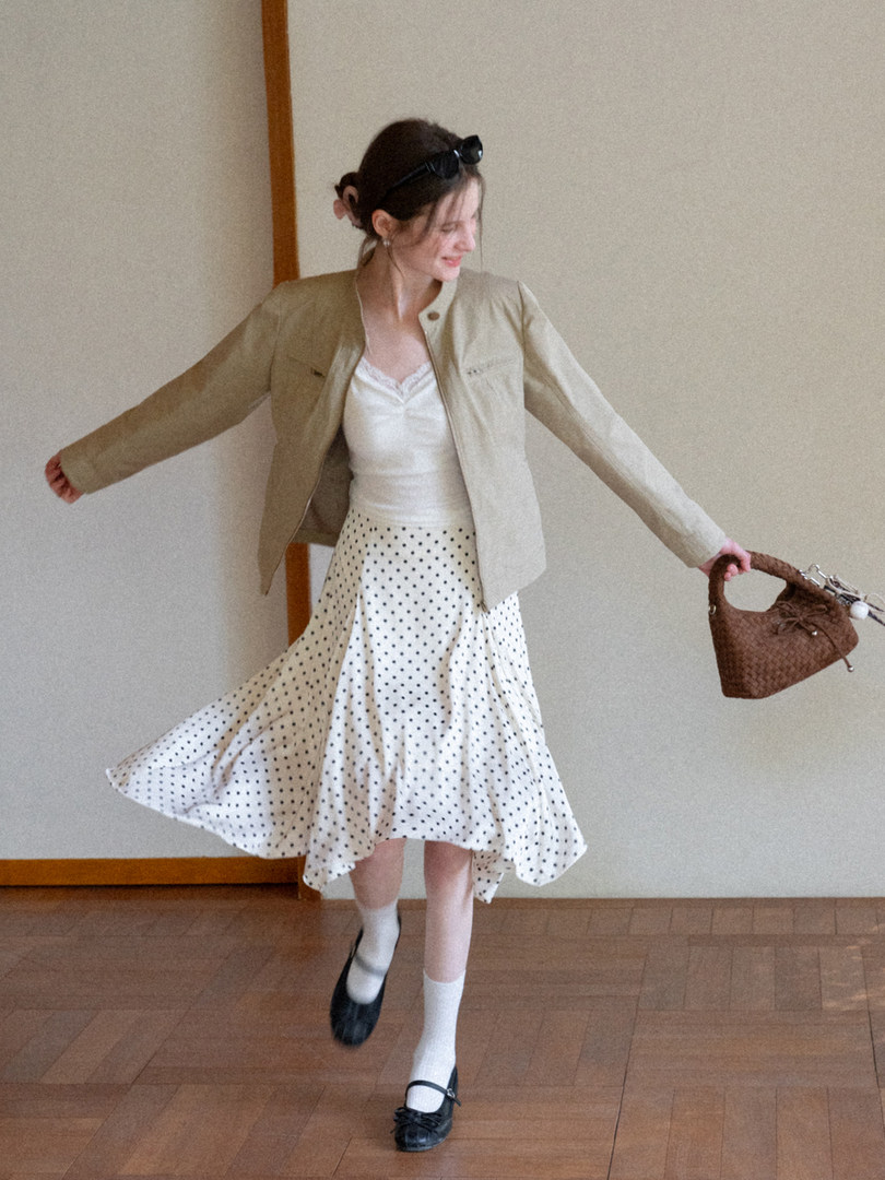 Model wearing a beige jacket with a white polka dot skirt and brown handbag