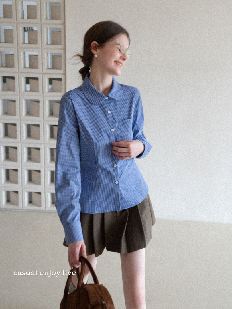 Woman wearing a blue button-up shirt with dark shorts and holding a brown handbag