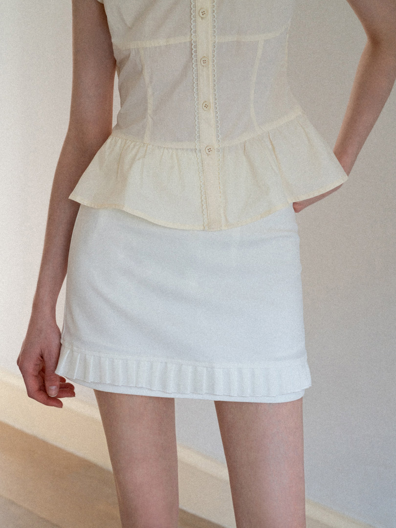 Model wearing a cream sleeveless button-front peplum top with a white mini skirt