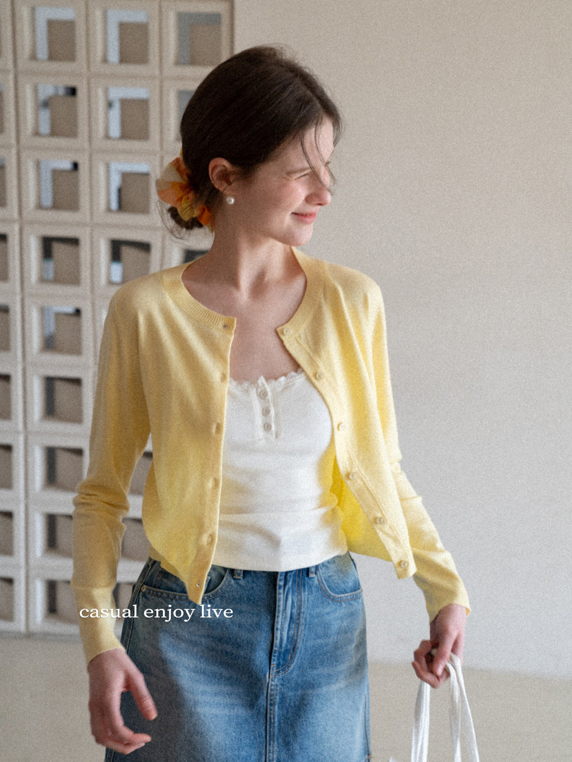 Woman wearing a light yellow button-front cardigan over a white tank top and jeans