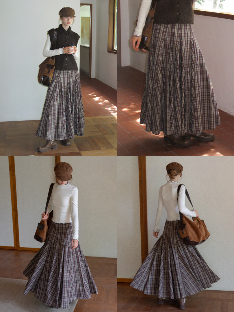Model wearing a plaid maxi skirt outfit with vest, long-sleeve top, cap, bag, and boots