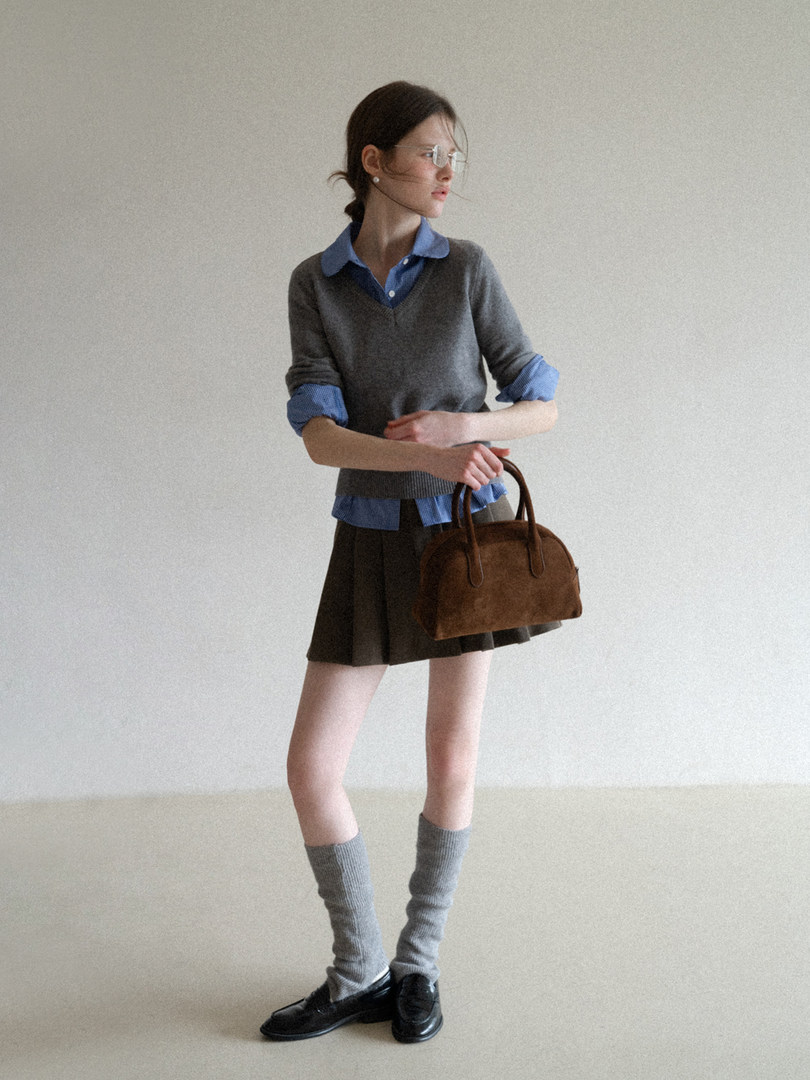 Model wearing a layered gray and blue preppy outfit with a brown handbag