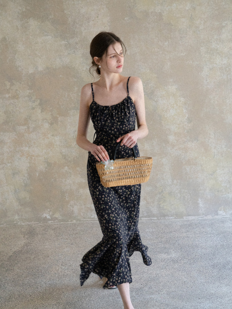 Woman wearing a black floral spaghetti-strap maxi dress and holding a woven basket bag