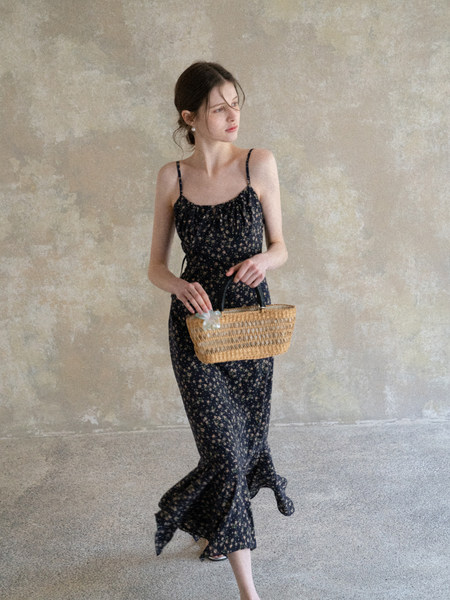 Woman wearing a black floral spaghetti-strap maxi dress and holding a woven basket bag