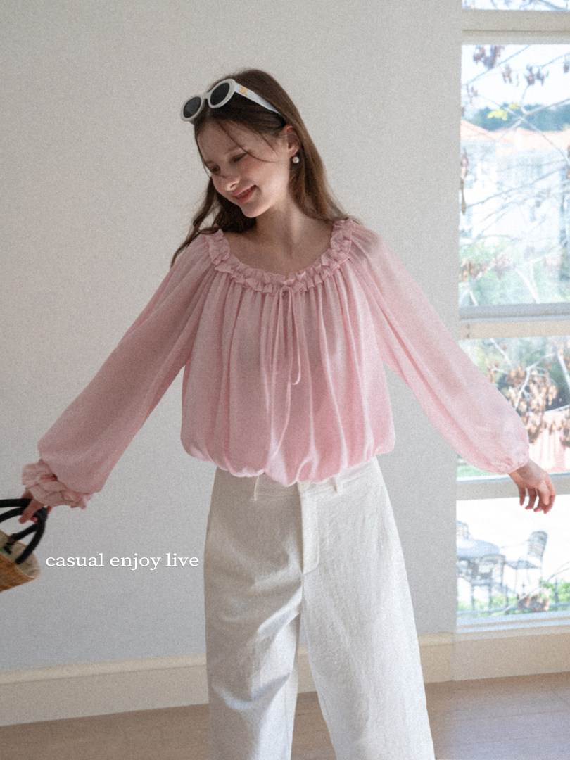 Model wearing a pink ruffled sheer blouse with white trousers