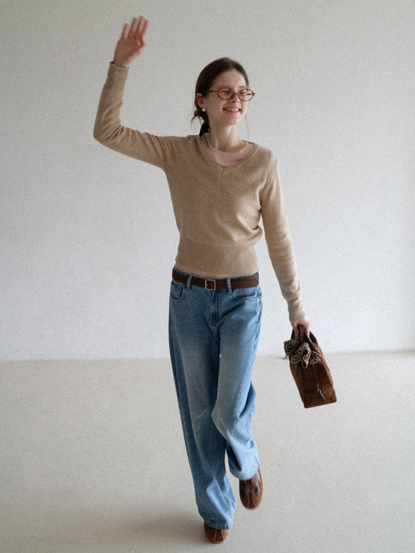 Woman wearing a beige sweater with blue jeans and holding a brown handbag