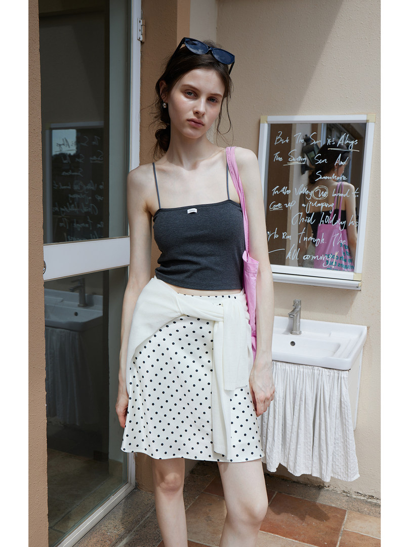 Model wearing a dark camisole top with a white polka dot skirt and pink shoulder bag