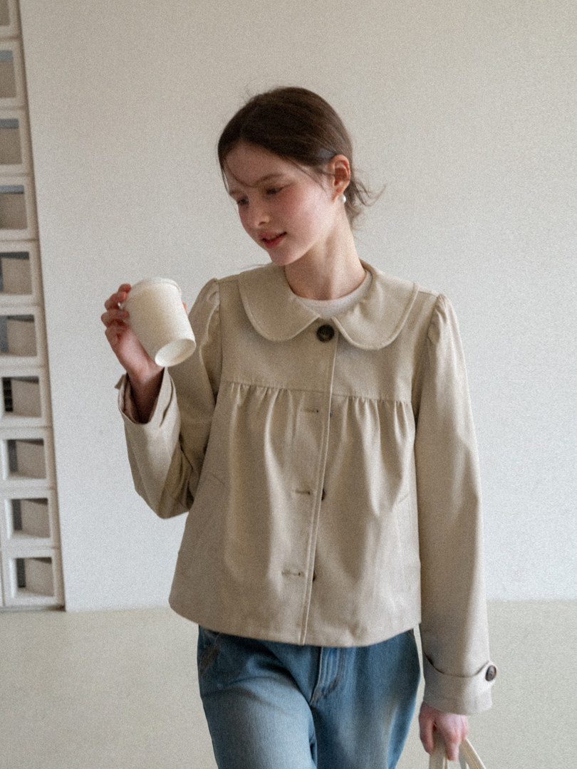 Woman wearing a beige Peter Pan collar jacket with blue jeans