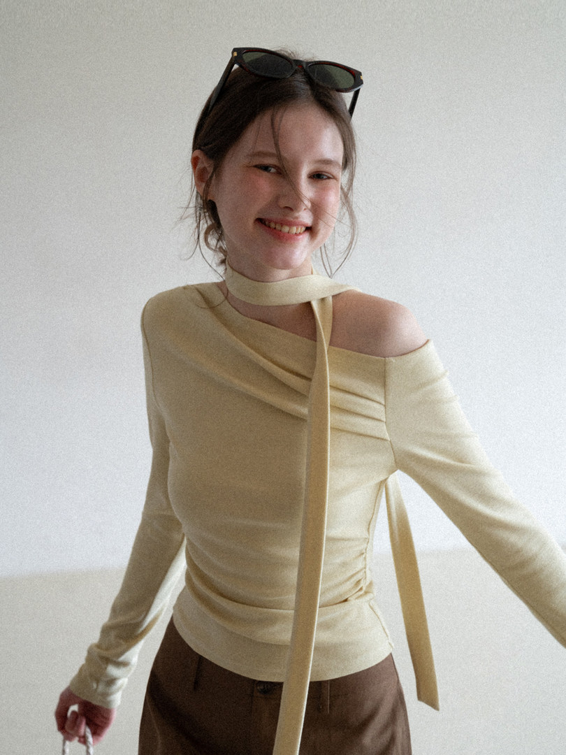 Model wearing a beige off-shoulder long-sleeve top with a tie detail