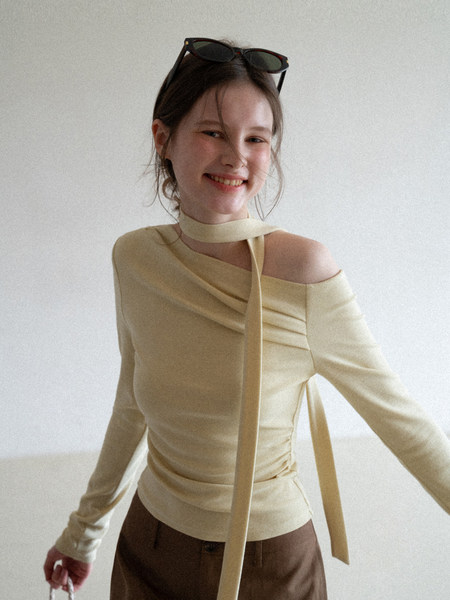 Model wearing a beige off-shoulder long-sleeve top with a tie detail