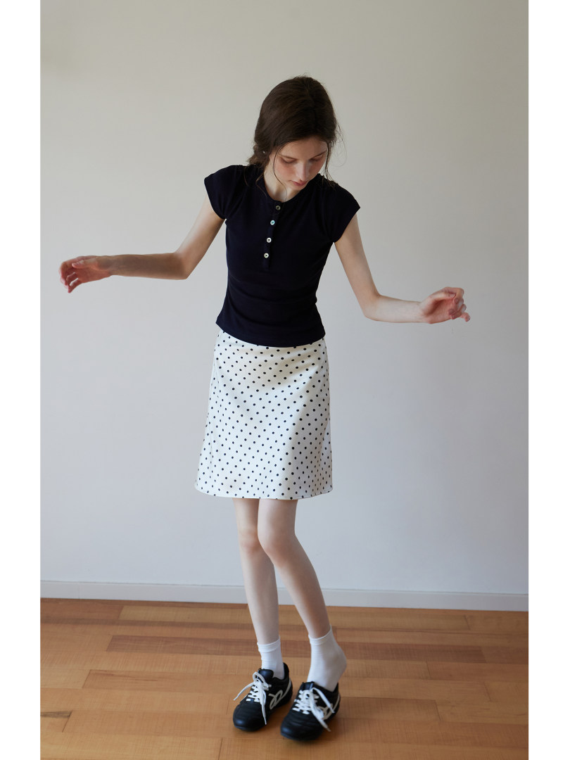 Model wearing a black short-sleeve top and a white polka dot skirt