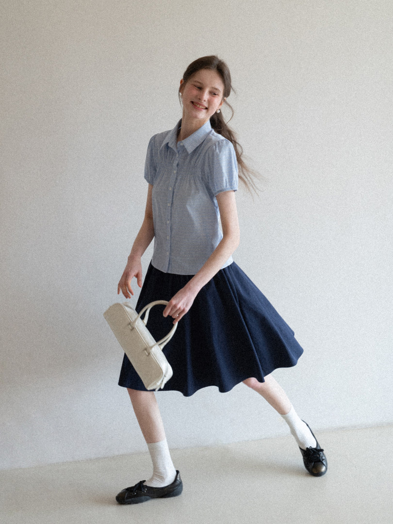 Woman modeling a light blue short-sleeve blouse with a navy skirt and cream handbag