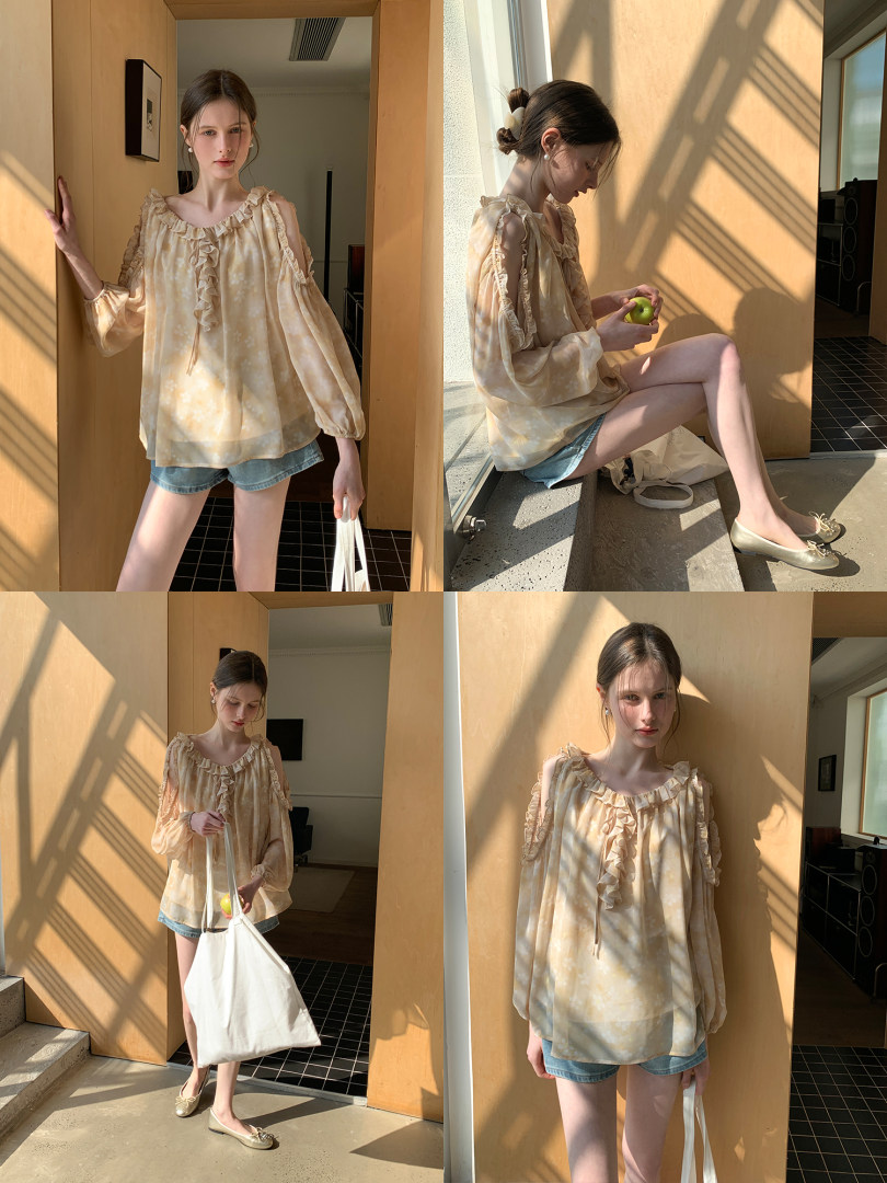Model wearing a light beige ruffled blouse with denim shorts in bright sunlight