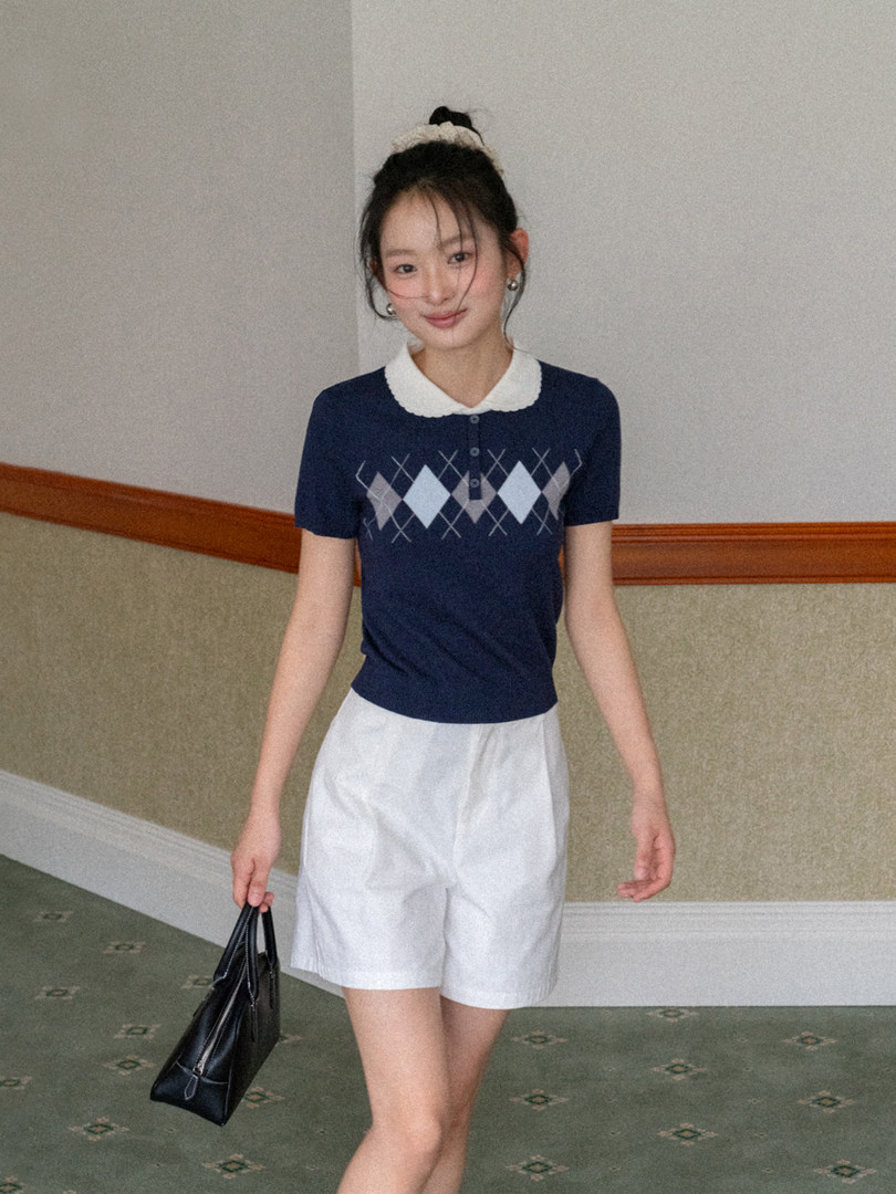 Model wearing a navy argyle short-sleeve polo top with white shorts and a black handbag