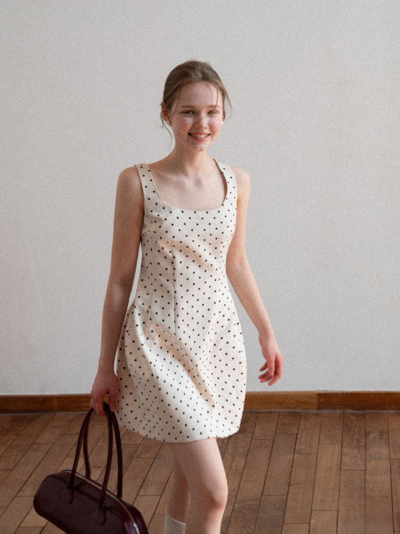 Woman wearing a white polka dot sleeveless dress and holding a brown handbag
