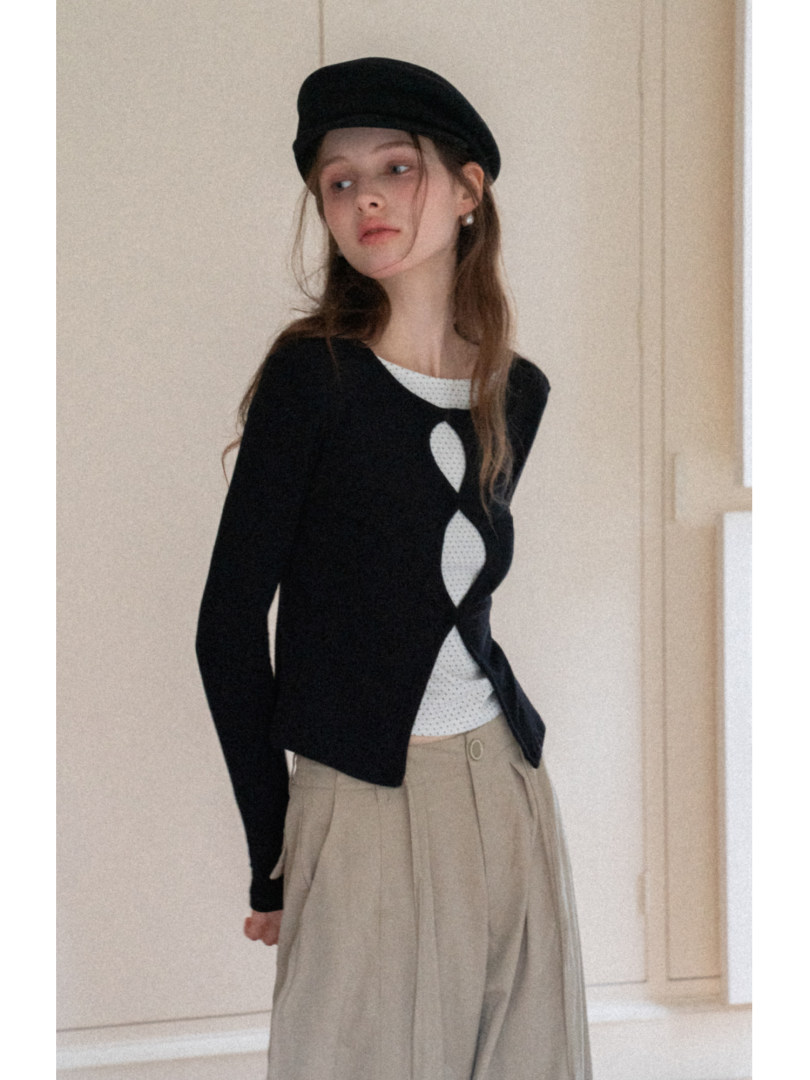 Model wearing a black long-sleeve top with a white layered insert and beige pleated trousers