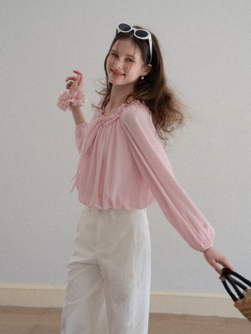 Model wearing a pink ruffled long-sleeve blouse with white pants