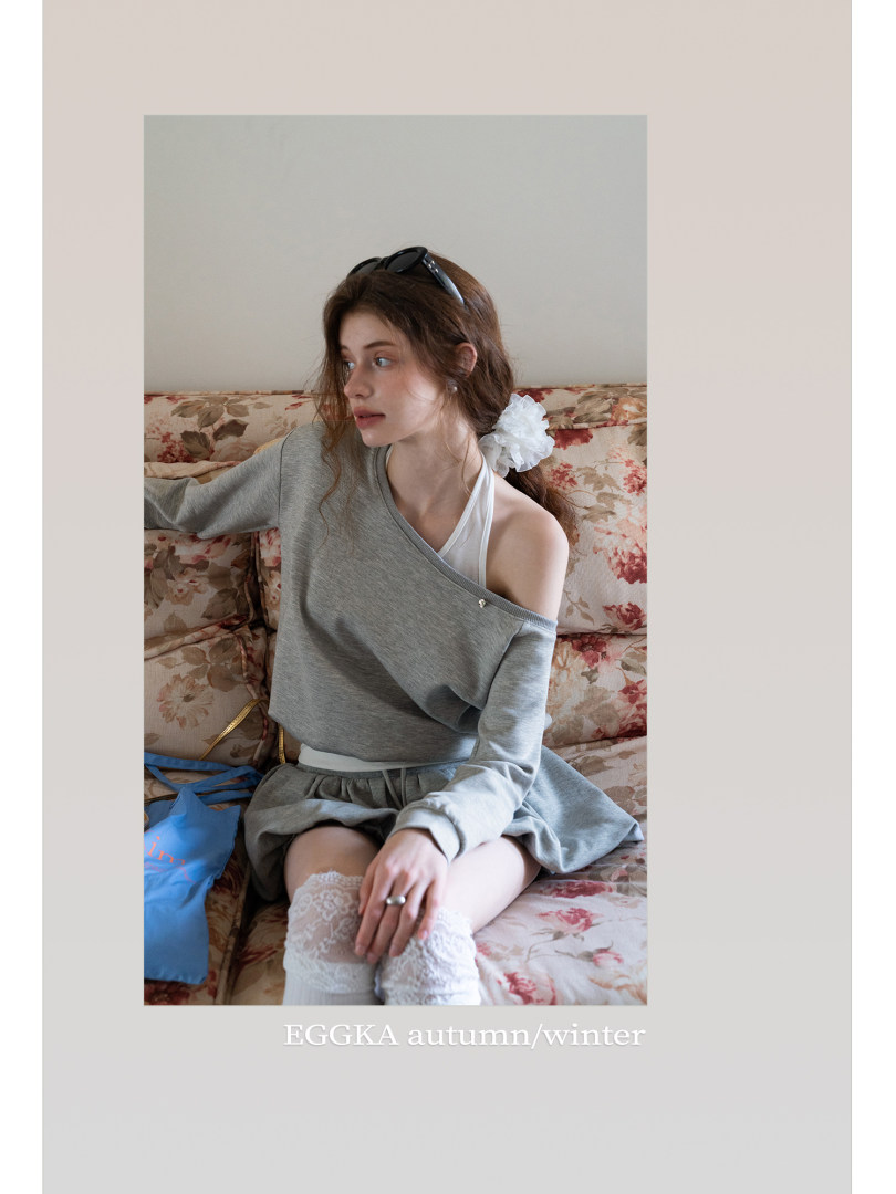Model wearing a gray off-shoulder sweatshirt and skirt on a floral sofa