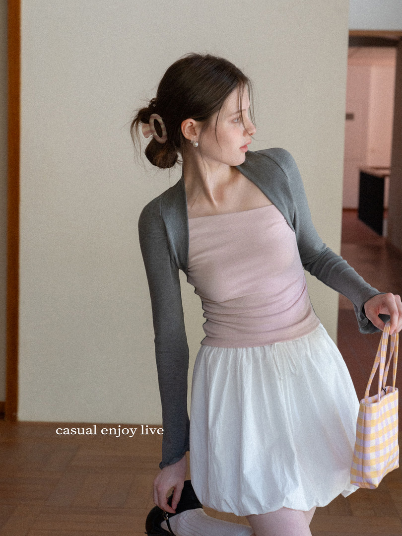 Woman wearing a pink camisole top with a gray long-sleeve shrug and a white skirt