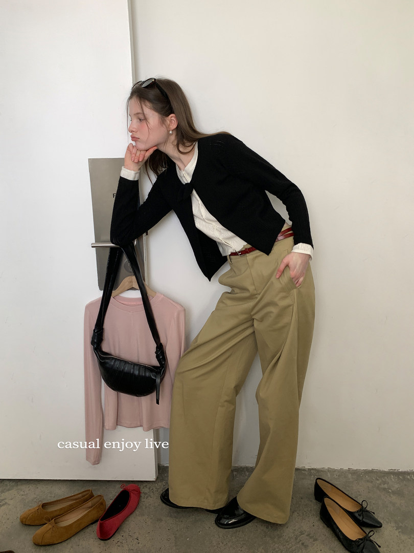 Model wearing a black cardigan with white blouse and wide-leg khaki trousers, styled with a black shoulder bag