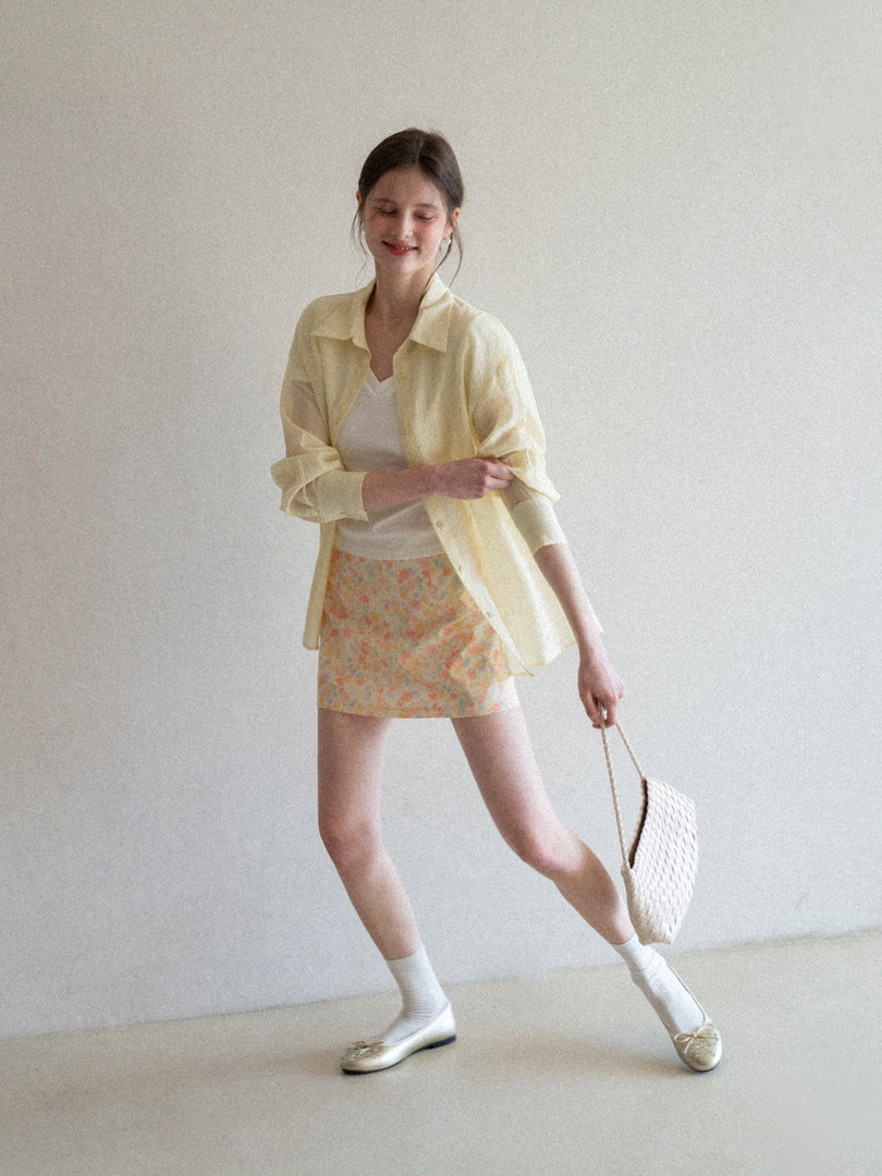 Woman modeling a light yellow shirt, white top, floral mini skirt, and woven handbag
