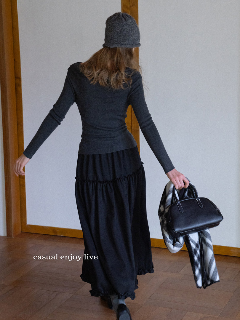 Woman wearing a dark casual outfit with beanie, carrying a black handbag and scarf