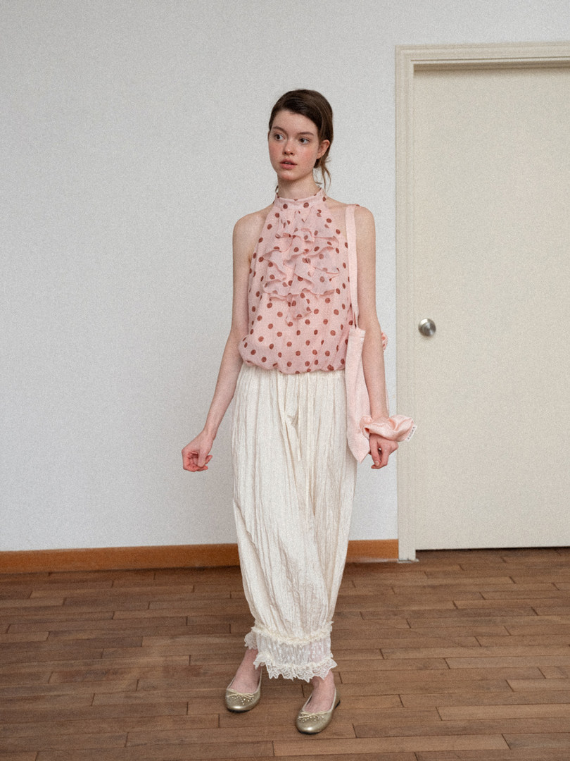 Model wearing a pink polka dot sleeveless top with cream loose pants and flats