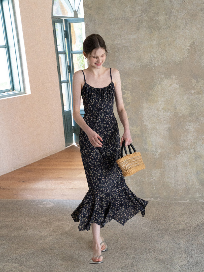 Woman wearing a black floral spaghetti-strap midi dress and holding a woven handbag