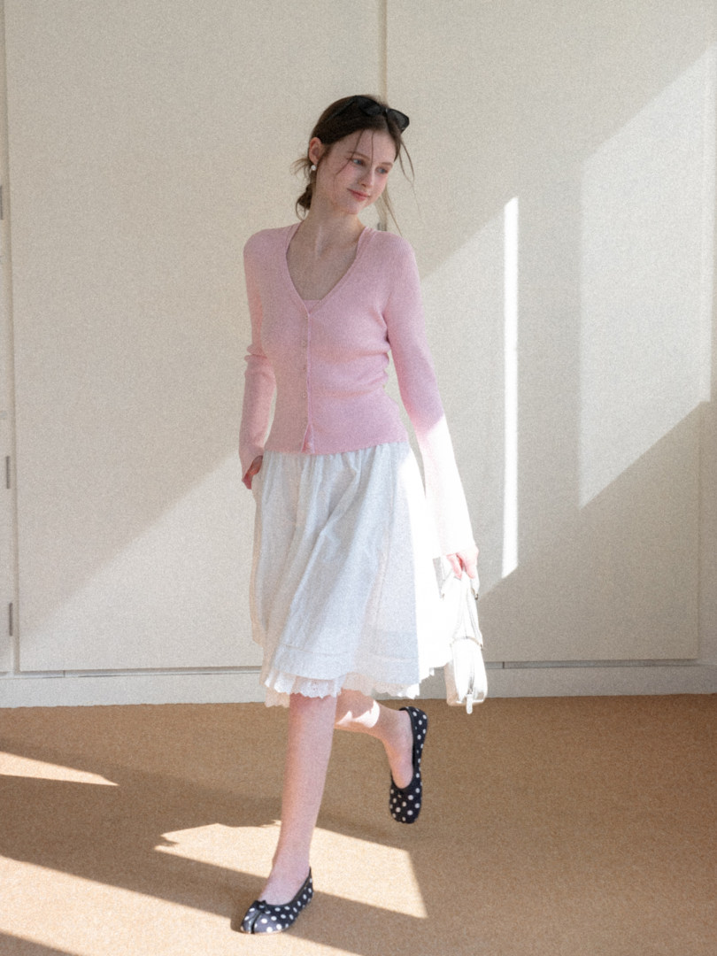 Model wearing a pink cardigan with a white skirt and polka dot flats