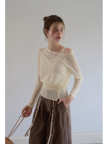Model wearing a cream sheer long-sleeve top with an off-shoulder neckline
