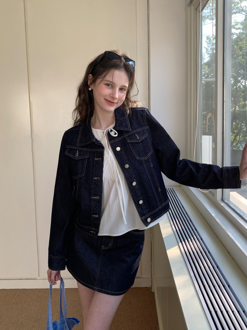 Woman wearing a dark denim jacket and matching mini skirt over a white blouse