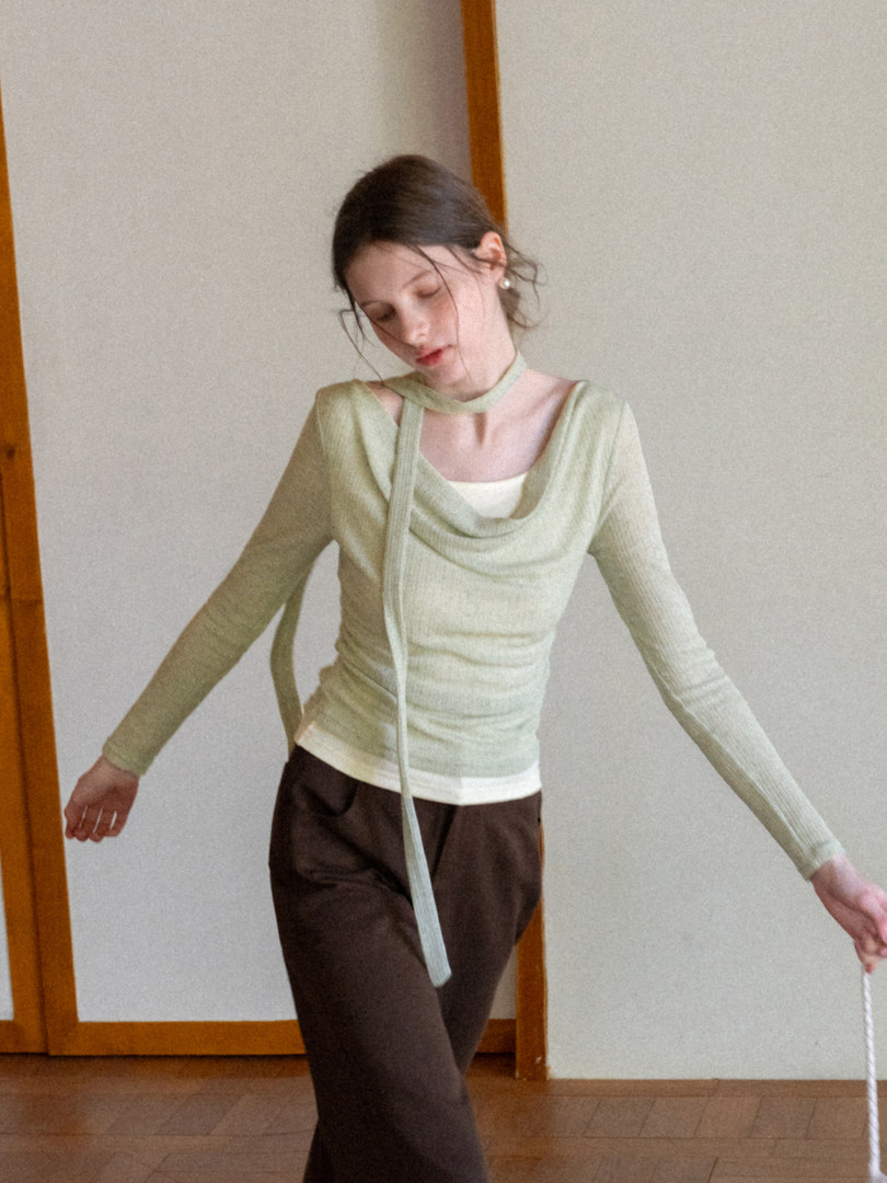 Woman wearing a light green long-sleeve draped top with dark pants